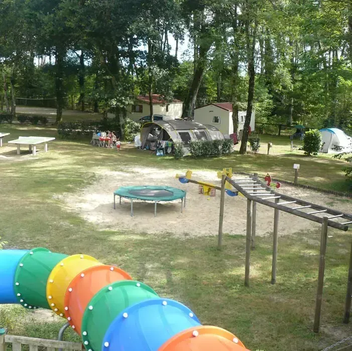 Aire de jeux avec tunnel coloré, trampoline et parcours en bois au milieu des emplacements de camping
