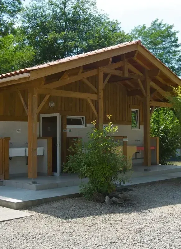 Bloc sanitaire en bois avec lavabos extérieurs dans un camping arboré