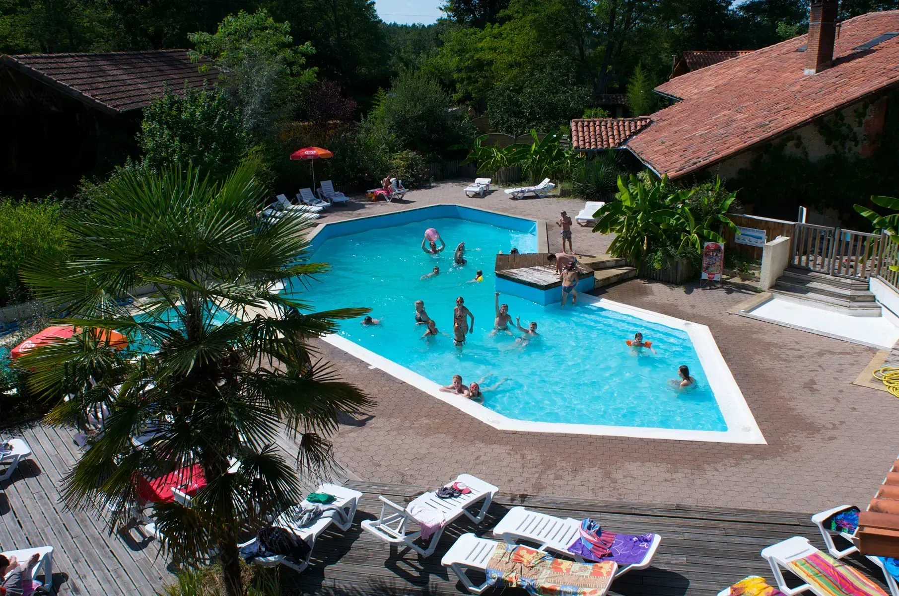 Vue en hauteur de la piscine avec des familles dans l’eau et des transats autour du bassin
