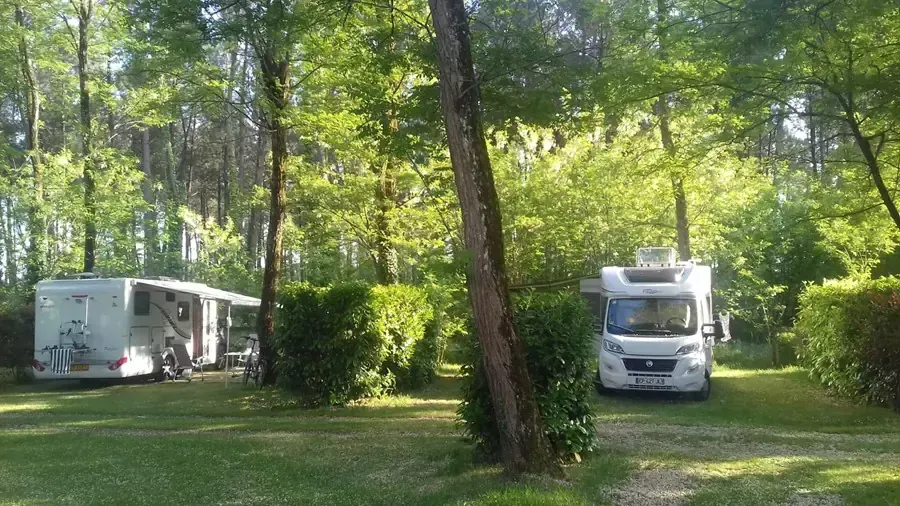 Deux camping-cars sur des emplacements herbeux ombragés et séparés par des haies