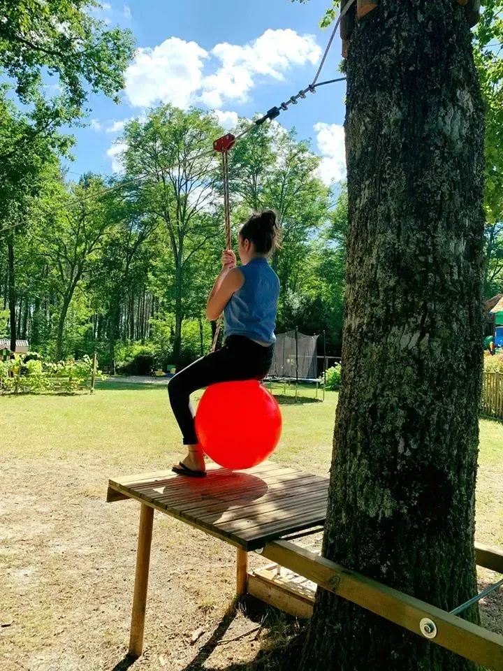 Jeune personne assise sur un ballon rouge utilisant une tyrolienne fixée à un arbre