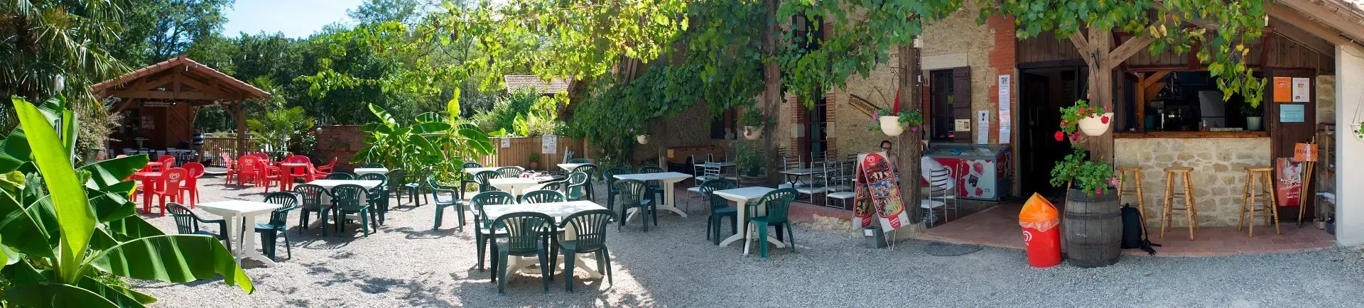 Terrasse panoramique du snack-bar avec tables et chaises au milieu de la végétation du camping