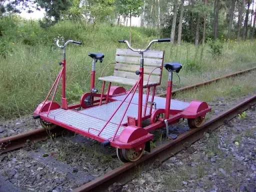 Vélorail rouge à deux postes sur une voie ferrée bordée d’herbes et d’arbres