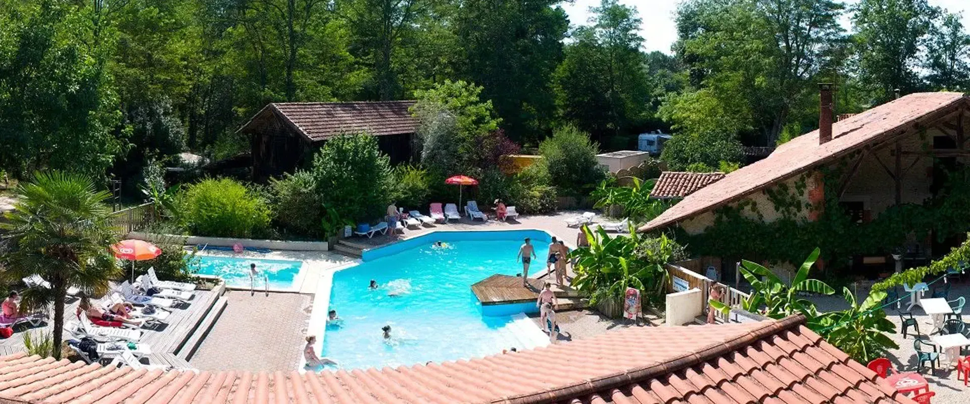 Piscine extérieure avec baigneurs au milieu des arbres et des bâtiments du camping