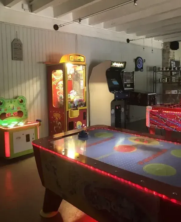 Salle de jeux avec table de air hockey, bornes d’arcade, machine à pince et jeu de fléchettes
