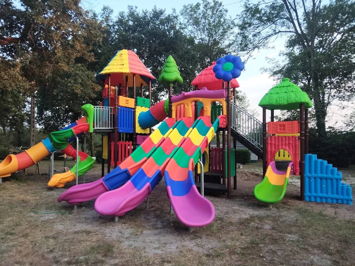 Aire de jeux avec tunnel coloré, trampoline et parcours en bois au milieu des emplacements de camping
