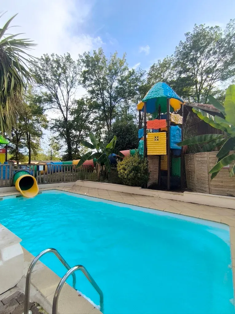 Toboggan aquatique coloré près du trampoline et des tables de ping-pong dans l’aire arborée